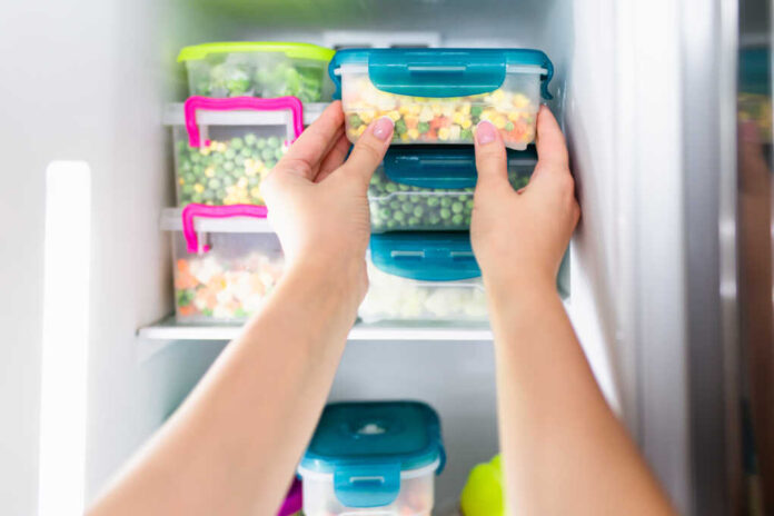 Woman,Placing,Container,With,Frozen,Mixed,Vegetables,In,Refrigerator.