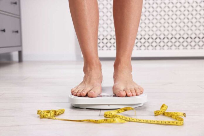 Woman,Standing,On,Floor,Scale,And,Measuring,Tape,At,Home,