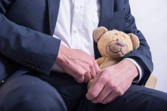 Older,Man,In,Suit,Snuggles,With,A,Stuffed,Animal,.