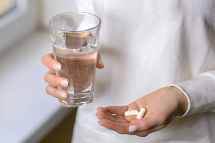 A,Woman,Holds,A,Glass,Of,Water,And,Two,Pills